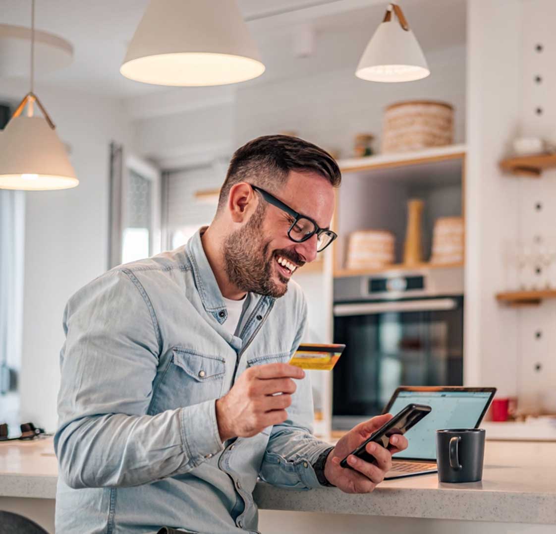 Man smiling while using a smartphone and holding a prepaid card, representing digital rewards with Best Payment Solutions