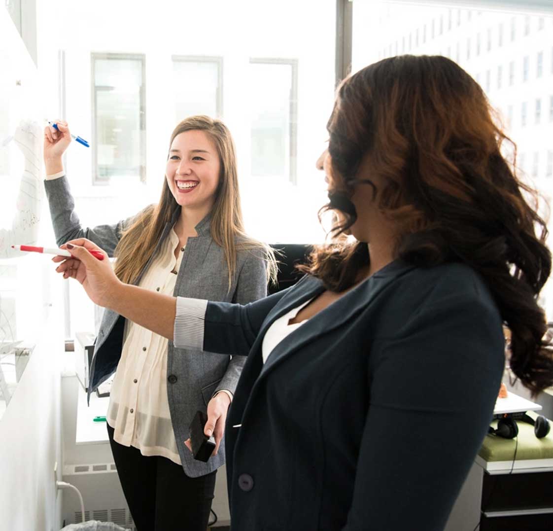 Two professional women smiling and collaborating at a whiteboard, representing team strategy and engagement with Best Payment Solutions
